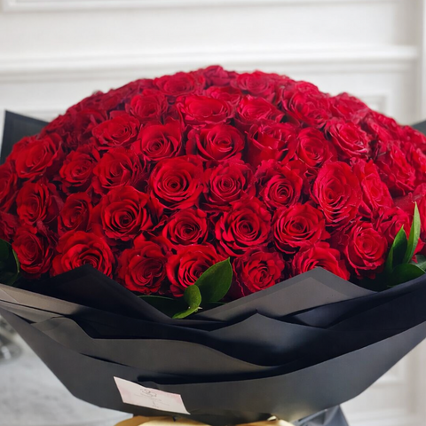 Luxury bouquet of 100 fresh red roses wrapped in black paper with gold ribbon, perfect for Valentine’s Day gifting in Abu Dhabi.