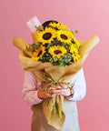 Person holding a bouquet of sunflowers against a pink background