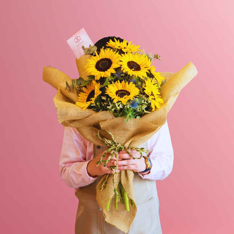 Person holding a bouquet of sunflowers against a pink background