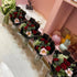 Decorative flowers in black containers on a pink shelf with various decor items.