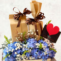 Two wrapped gifts with brown ribbons, a bouquet of blue flowers, and a red heart card on a light background.
