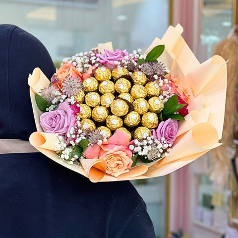 Bouquet of flowers with gold Ferrero Rocher chocolates held by a person.