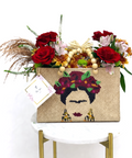 Woven handbag with Frida Kahlo design and floral arrangement on a white surface