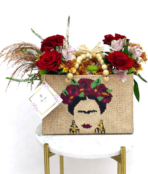 Woven handbag with Frida Kahlo design and floral arrangement on a white surface