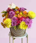 Colorful bouquet of flowers in a woven basket on a small round table with a light pink background