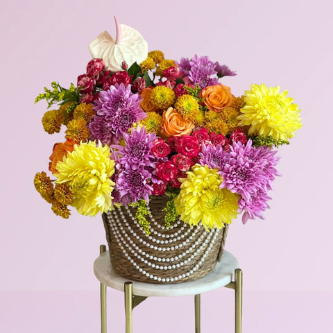 Colorful bouquet of flowers in a woven basket on a small round table with a light pink background