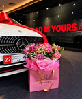 Pink rose bouquet in a Danaya’s Flowers gift bag beside a white Mercedes decorated with red ribbon.