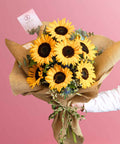 Bouquet of sunflowers wrapped in brown paper with a pink background