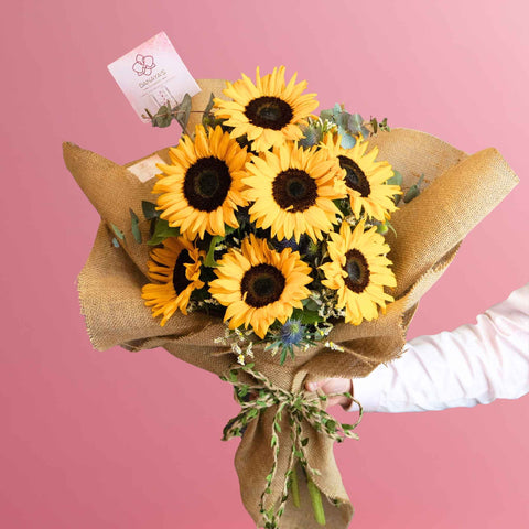 Bouquet of sunflowers wrapped in brown paper with a pink background
