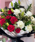 Bouquet of red and white flowers held by an Emirati person in a white outfit.