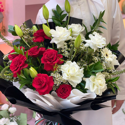 Bouquet of red and white flowers held by an Emirati person in a white outfit.