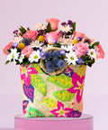 Colorful floral arrangement in a patterned bag on a pink background