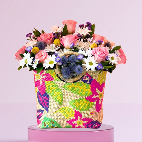 Colorful floral arrangement in a patterned bag on a pink background