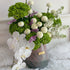 Floral arrangement with white and green flowers in a vase on a white surface