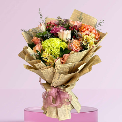 Bouquet of flowers wrapped in newspaper with a pink ribbon on a pink background