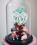 Decorative display with figurines under a glass dome featuring floral elements and a 'LOVE' heart.