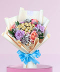Bouquet of flowers with ferrero chocolate  wrapped in paper and tied with a blue ribbon on a pink background