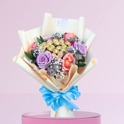 Bouquet of flowers with ferrero chocolate  wrapped in paper and tied with a blue ribbon on a pink background