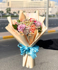 Bouquet of flowers with a blue ribbon held by a person outdoors.