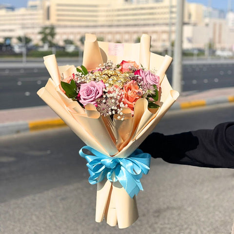 Bouquet of flowers with a blue ribbon held by a person outdoors.