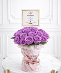 Bouquet of purple roses in a decorative vase with a 'DANAYAS' card on a white background