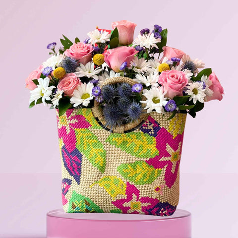 Colorful woven bag filled with flowers on a pink background