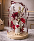 Decorative angel figure with red heart and flowers under a glass dome on a marble surface.