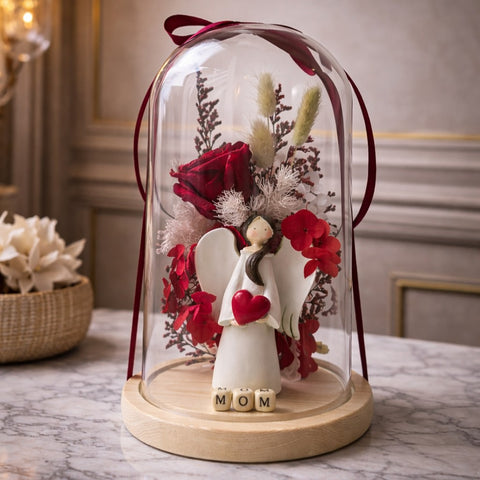 Decorative angel figure with red heart and flowers under a glass dome on a marble surface.