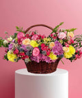 Basket of colorful flowers on a white pedestal against a pink background