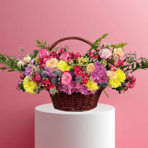 Basket of colorful flowers on a white pedestal against a pink background