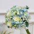Bouquet of blue and green flowers in a clear vase on a white background