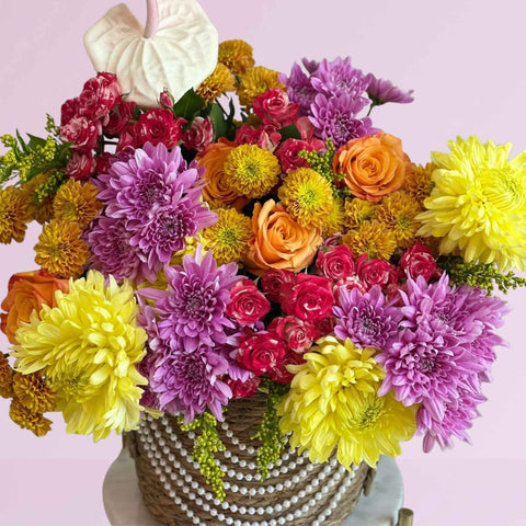 Colorful bouquet of flowers in a woven basket on a light pink background