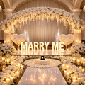Decorated stage with 'MARRY ME' sign, flowers, and candles in a grand hall, Abu Dhabi.