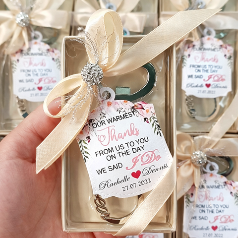 Love infinity bottle opener with ribbon and decorative tag held by a hand, with more party favors in the background.