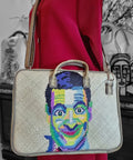 Handbag with a colorful portrait design held by a person wearing a red coat.