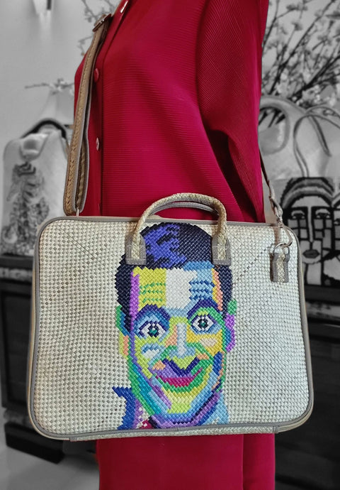 Handbag with a colorful portrait design held by a person wearing a red coat.