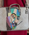 Handbag with a colorful face design held by a person wearing a red garment.