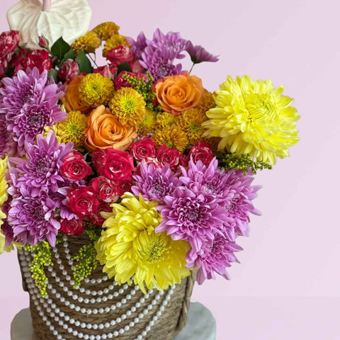 Colorful bouquet of flowers in a woven basket on a pink background