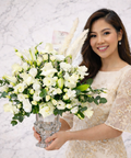 An elegant white floral arrangement in a crystal vase, styled on a white marble background for a timeless and luxurious finish. A woman holding it.
