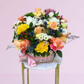 Colorful flower arrangement in a basket on a small table with a pink background