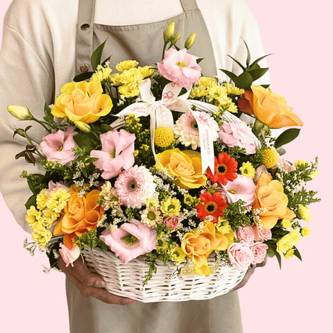 Person holding a basket of colorful flowers against a pink background