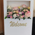 Floral arrangement on a 'Welcome' sign with a white frame