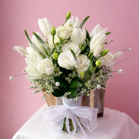 Ivory white bridal bouquet with roses and soft floral accents, finished with lace ribbon – elegant wedding bouquet Abu Dhabi.